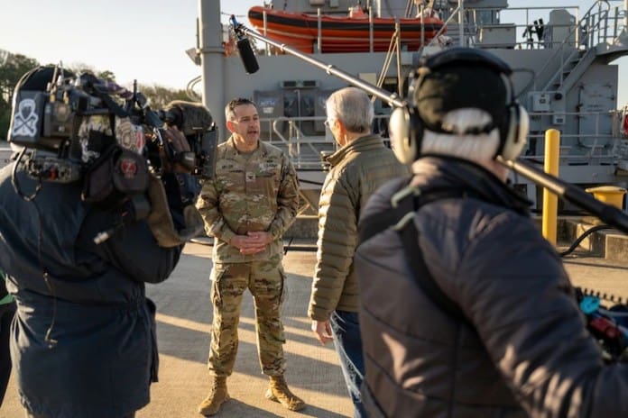 Un soldado uniformado habla con un equipo de cámara en un muelle.