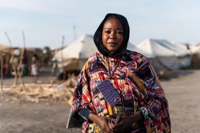 A woman in a colourful dress stands in front of rows of white tents in an IDP camp. A woman in a colourful dress stands in front of rows of white tents in an IDP camp.